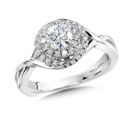 The center stone’s first halo perfectly frames the diamond with a unified circular shape. The second halo crisscrosses from the shank below, transforming into two separate diamond bands that nearly look like one. The crisscross style of the golden shank p